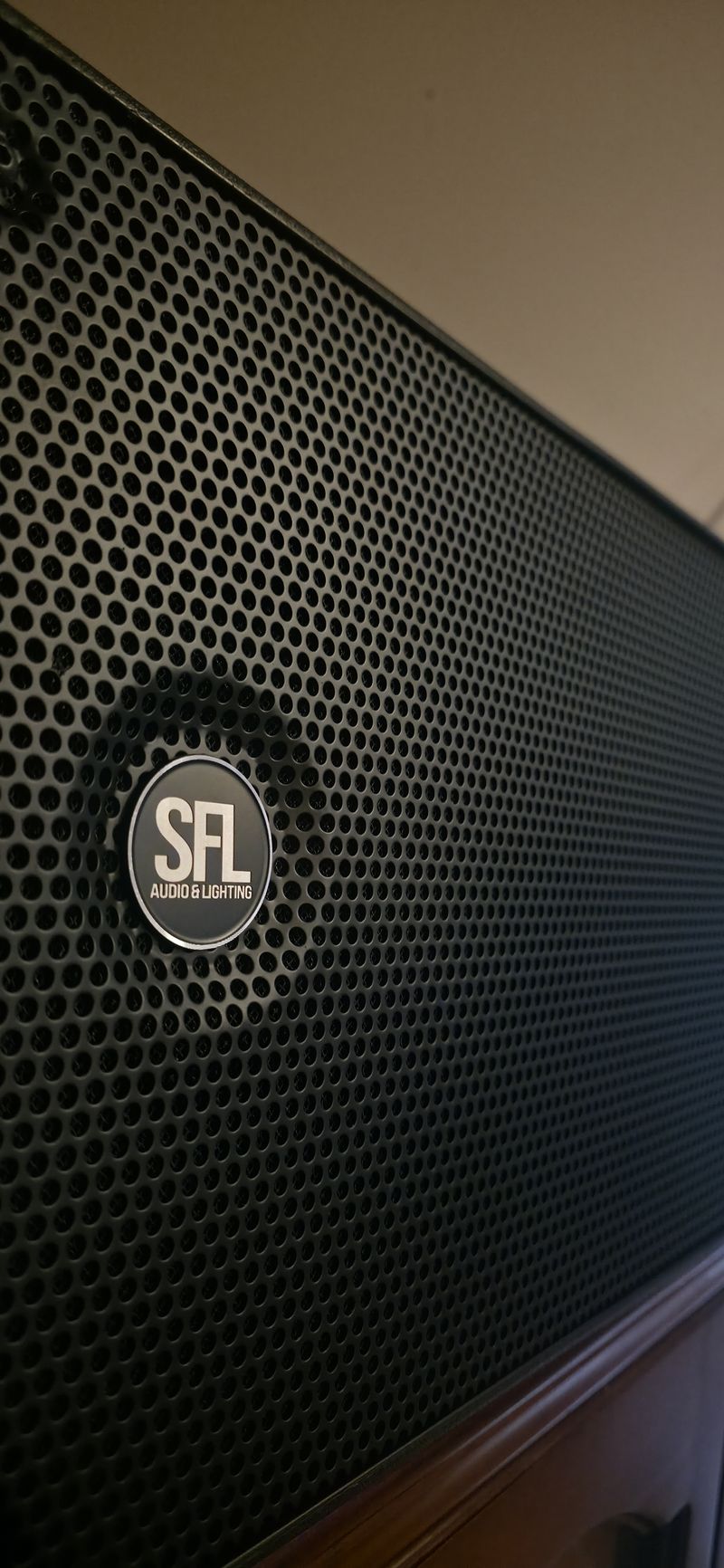 Close-up of an SFL Audio & Lighting speaker grille with its round metal badge